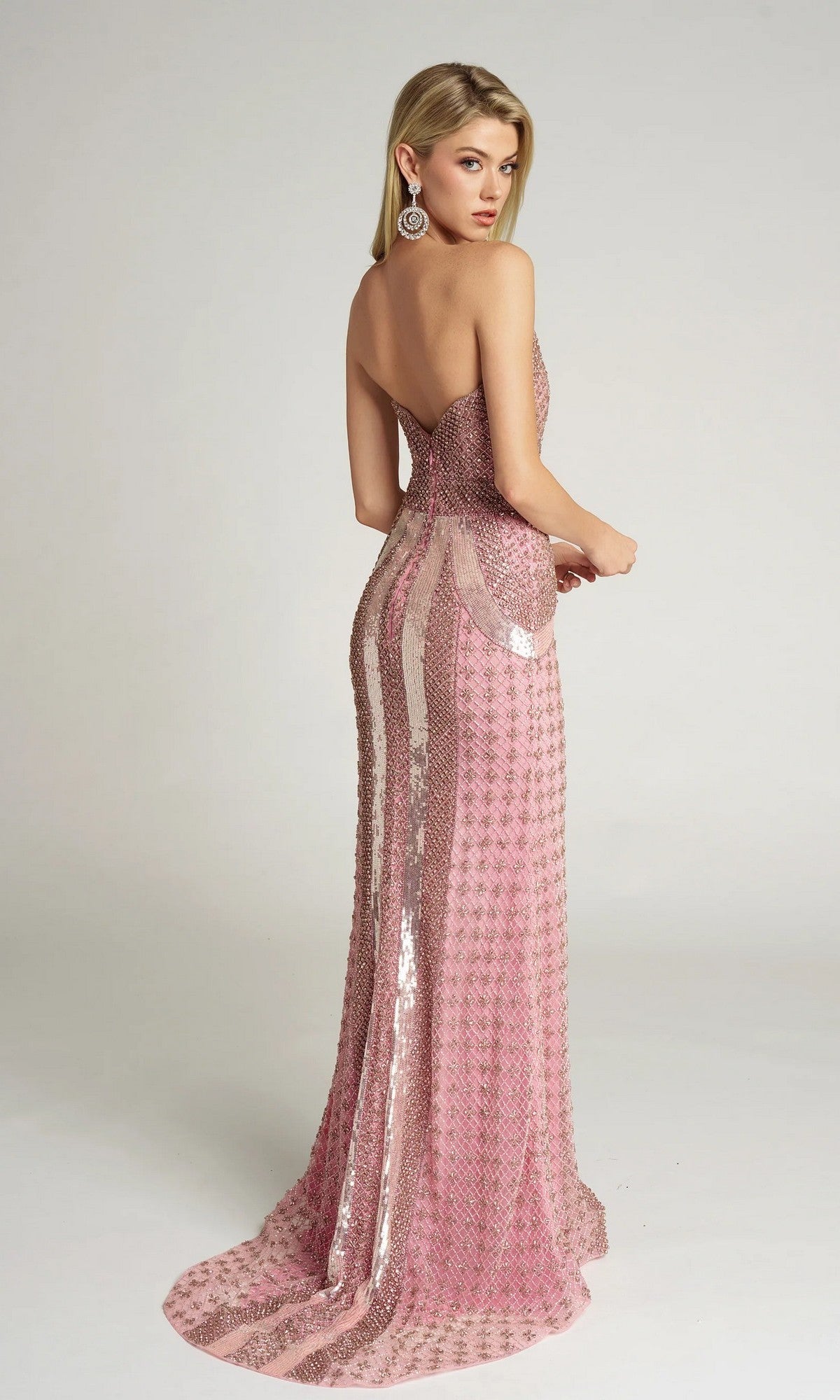 A woman wears the Portia and Scarlett PS25986C long formal dress—strapless, floor-length, fitted, and embellished with pink sequins—stands facing away, looking over her shoulder against a plain light background.
